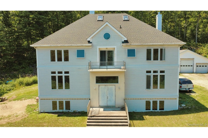 View of front facade with a chimney, a balcony, a front yard, and a garage