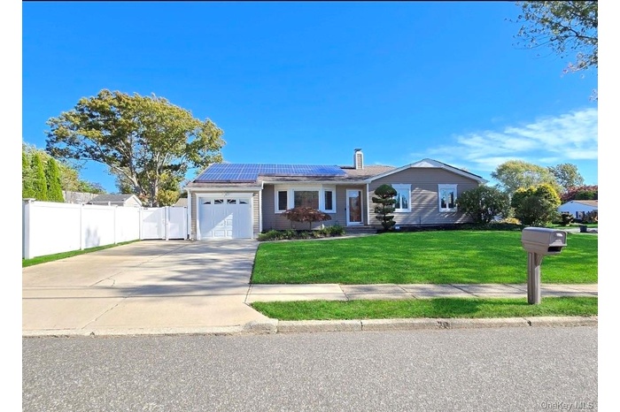 Ranch-style house featuring roof mounted solar panels, concrete driveway, an attached garage, a chimney, and a gate