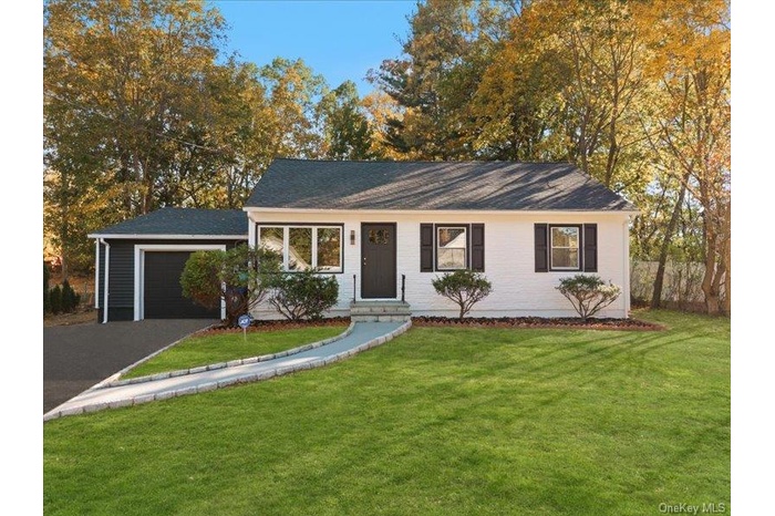 Single story home featuring a front lawn, asphalt driveway, an attached garage, a shingled roof, and view of wooded area
