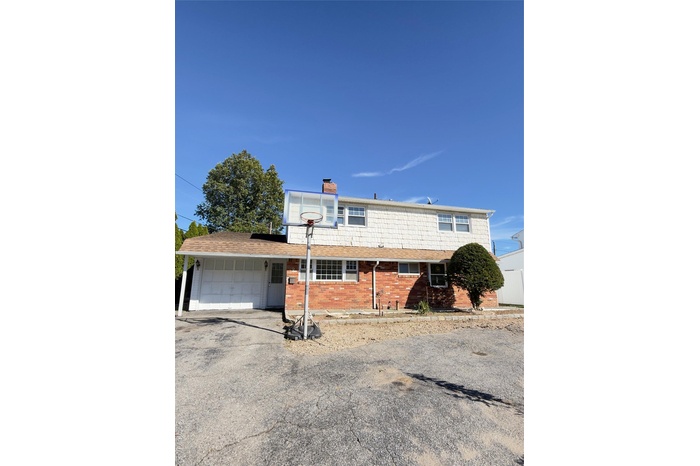 View of front of home with brick siding, a chimney, driveway, and an attached garage