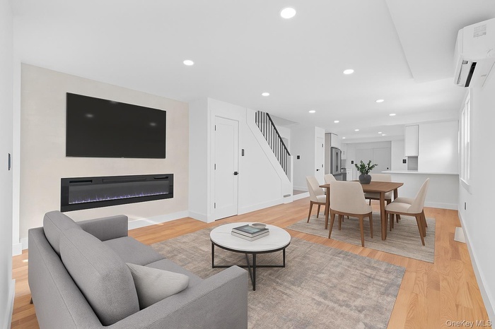Living area with a glass covered fireplace, light wood-style flooring, recessed lighting, a wall unit AC, and stairway