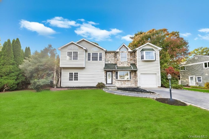 Traditional-style home featuring asphalt driveway, a front yard, stone siding, and an attached garage