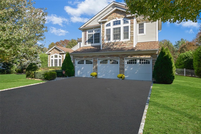 View of front of property featuring stone siding, a garage, and asphalt driveway