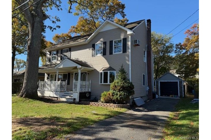 View of front facade with a detached garage, a front lawn, an outbuilding, covered porch, and a chimney