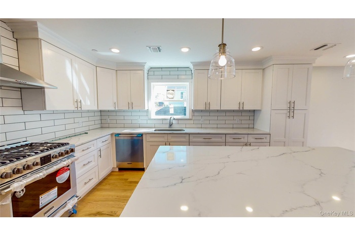 Kitchen featuring appliances with stainless steel finishes, light stone counters, decorative light fixtures, wall chimney exhaust hood, and recessed l