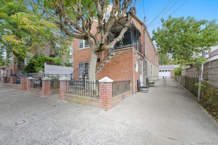 View of side of property featuring a balcony, brick siding, a fenced front yard, and a gate