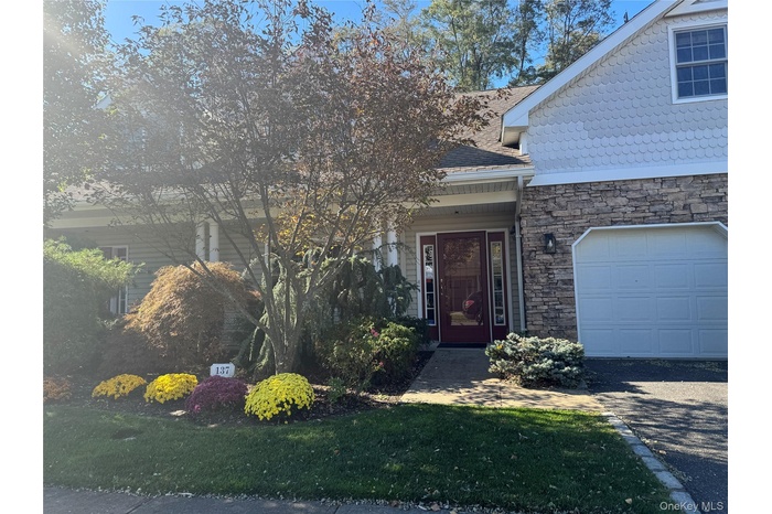 Entrance to property with a garage, stone siding, driveway, and a lawn
