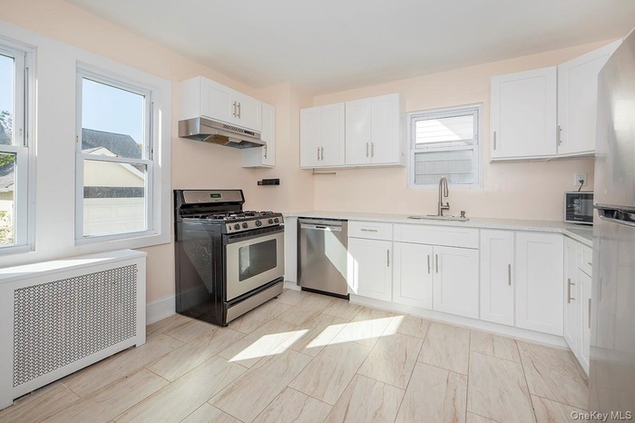 Kitchen with stainless steel appliances,  white cabinetry, under cabinet range hood, and light stone counters