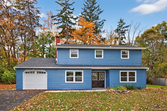 Traditional-style home featuring driveway, a chimney, an attached garage, and roof with shingles