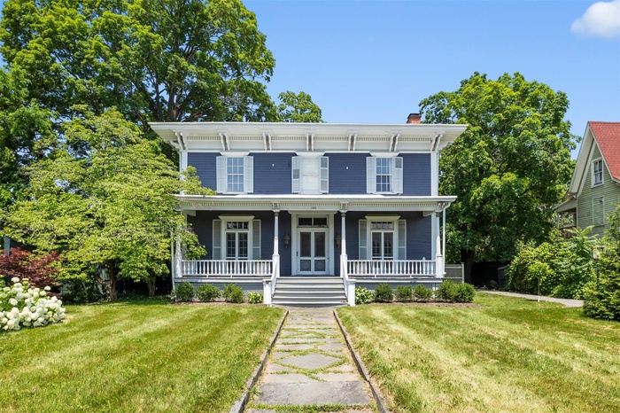 Italianate house featuring a chimney, a front lawn, and covered porch