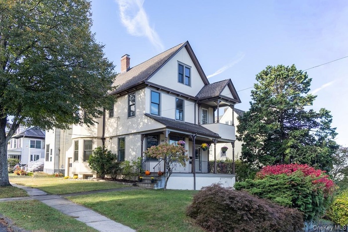 View of front of home with stucco siding, a chimney, a front yard, and a porch