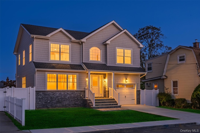 View of front of home with stone siding, driveway, roof with shingles, and covered porch