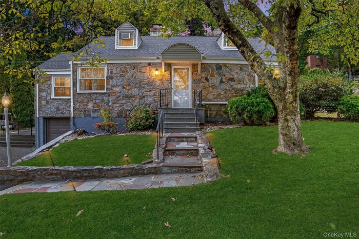 Cape cod home with stone siding, a front yard, and an attached garage