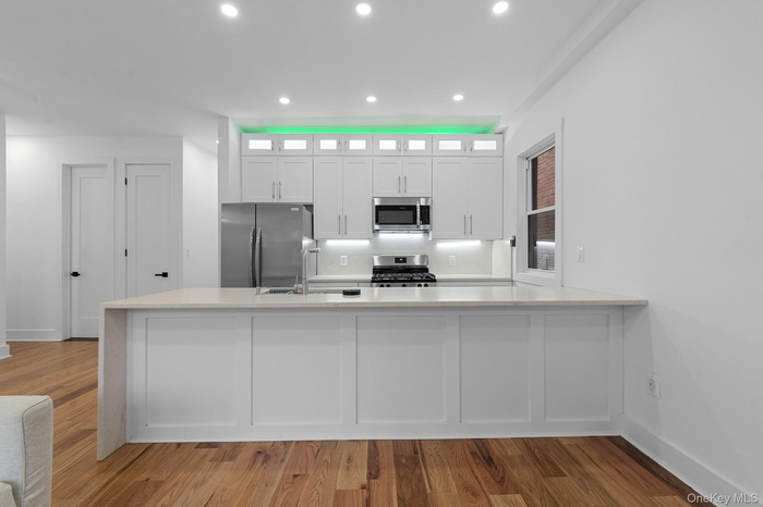 Kitchen featuring appliances with stainless steel finishes, glass insert cabinets, white cabinetry, a peninsula, and light wood-type flooring