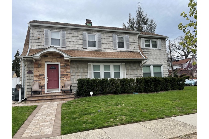 View of front of property with a front lawn, a chimney, and stone siding