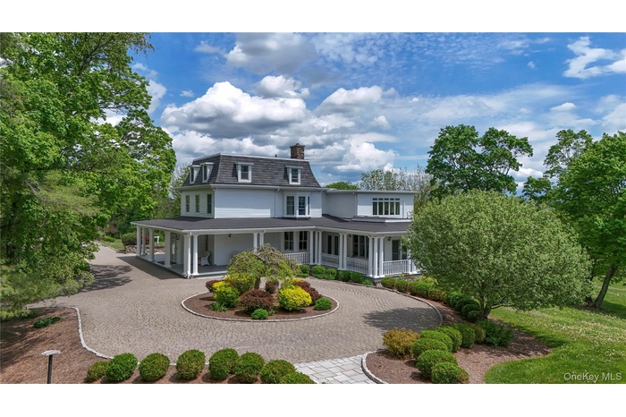 Back of house featuring curved driveway, covered porch, a chimney, and mansard roof