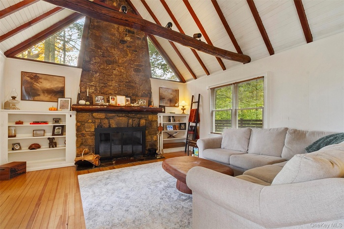 Living area with a fireplace, high vaulted ceiling, wood-type flooring, and beam ceiling