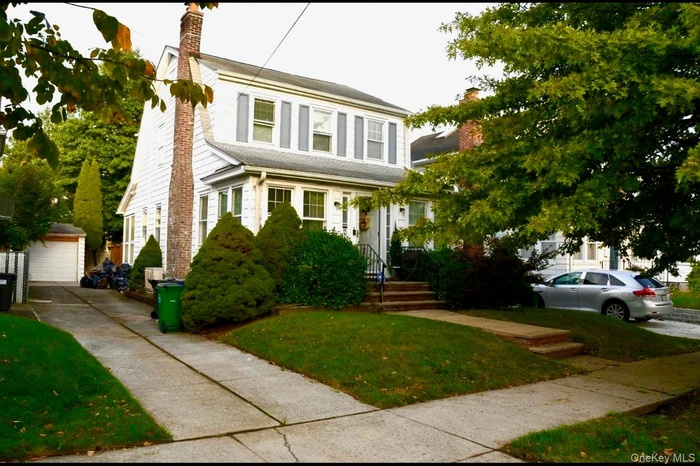 View of front of home featuring an outbuilding, a chimney, a front yard, and a garage