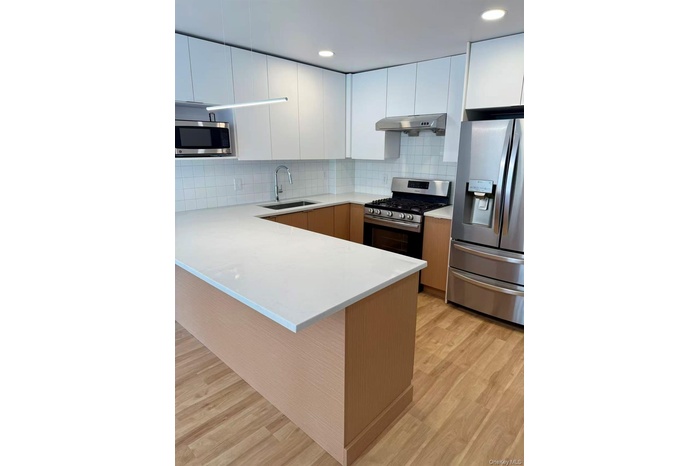 Kitchen with stainless steel appliances, modern cabinets, a peninsula, white cabinets, and light wood-type flooring