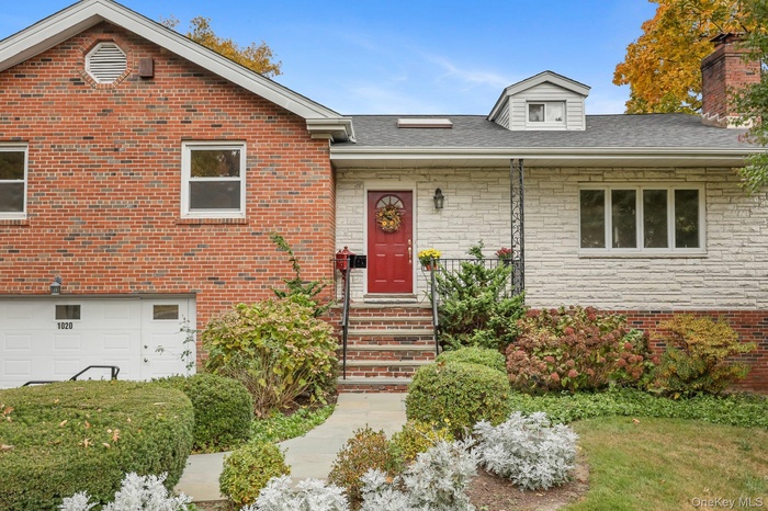 View of front facade featuring a chimney, a shingled roof, brick siding, and stone siding