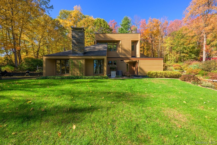 Back of house with a yard, a chimney, and a wooded view