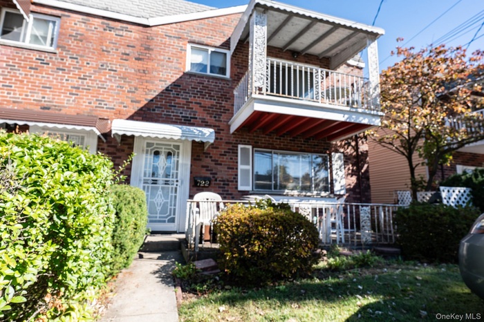 View of front of home featuring brick siding, a balcony, and a front lawn