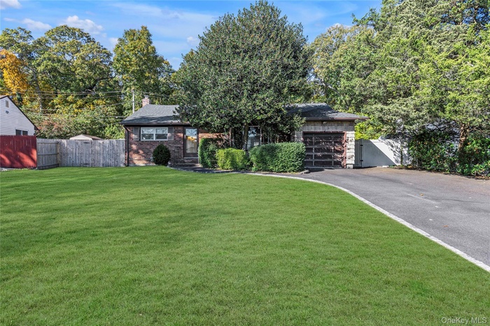 View of front of house with asphalt driveway, brick siding, an attached garage, a chimney, and view of scattered trees