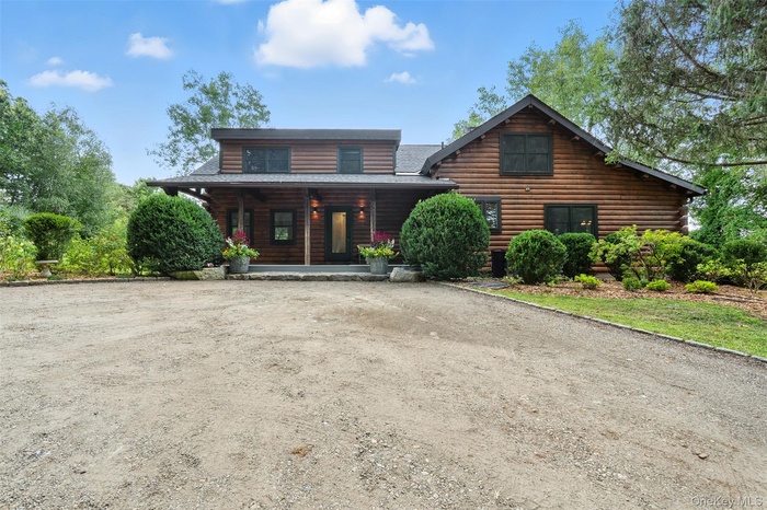 Log cabin with log exterior, covered porch, and a shingled roof