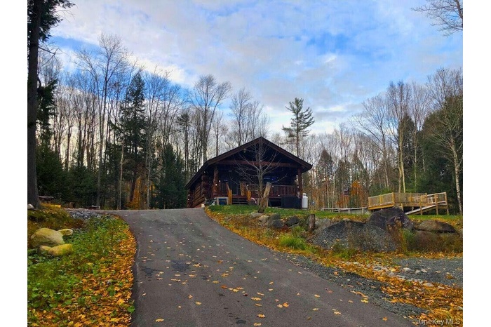 View of front of house with a deck, a forest view, and asphalt driveway