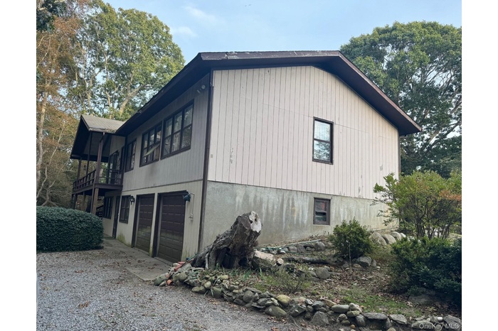 View of home's exterior with an attached garage, gravel driveway, and a balcony