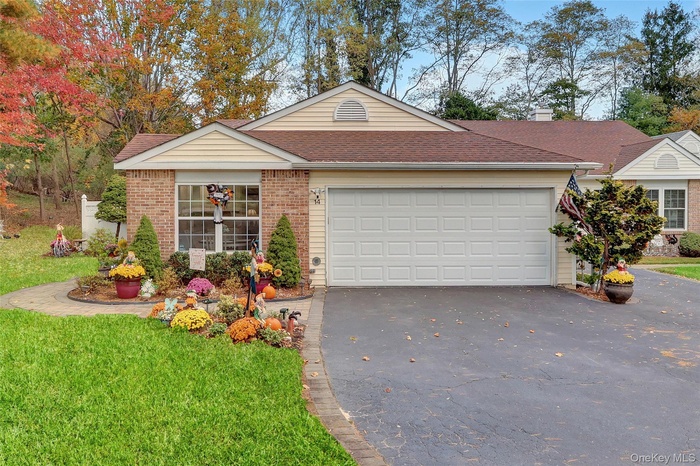 Ranch-style home featuring asphalt driveway, a shingled roof, brick siding, an attached garage, and a front yard