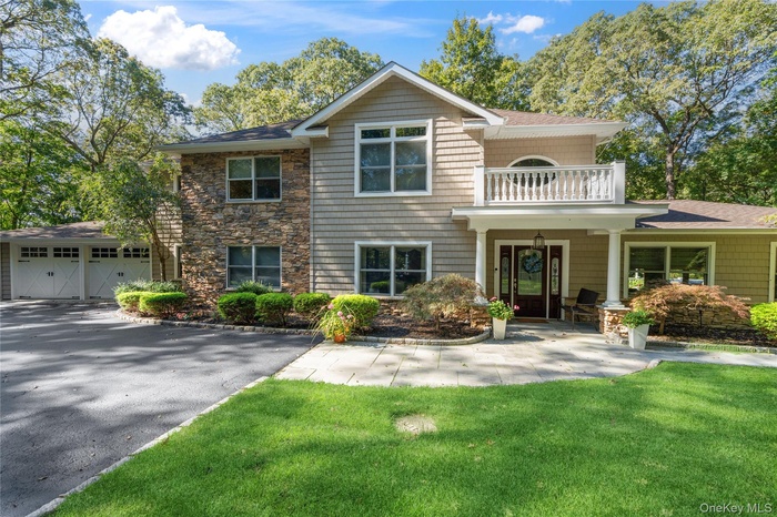 View of front facade with a balcony, a front lawn, a garage, and a patio area