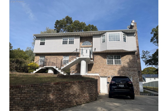 Bi-level home with stairs, driveway, a garage, a chimney, and brick siding