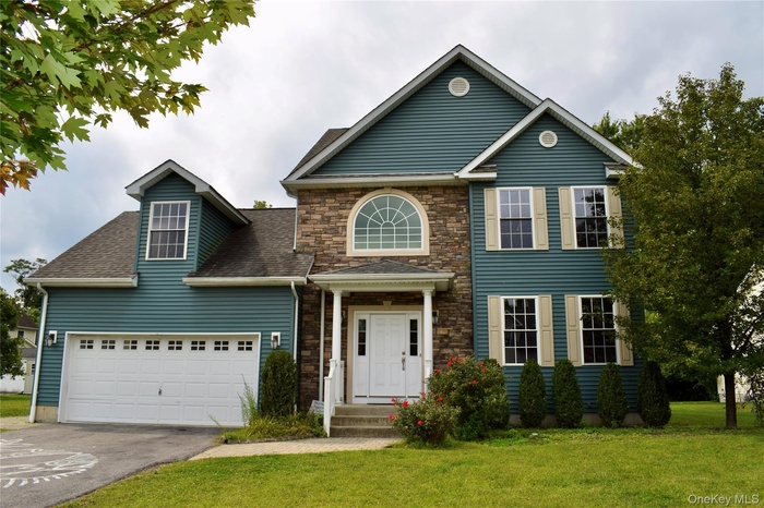 View of front facade featuring a front lawn, asphalt driveway, a garage, stone siding, and a shingled roof