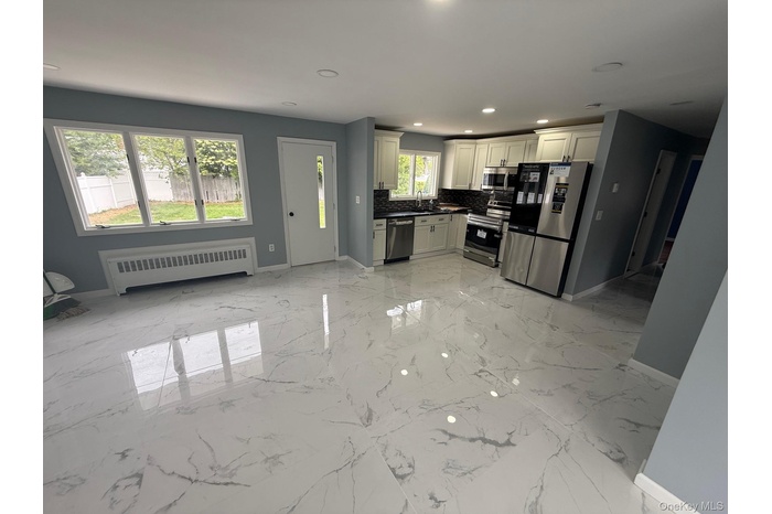 Kitchen featuring appliances with stainless steel finishes, dark countertops, recessed lighting, radiator heating unit, and light marble finish floori