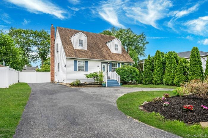Cape cod-style house featuring driveway, a chimney, and a shingled roof