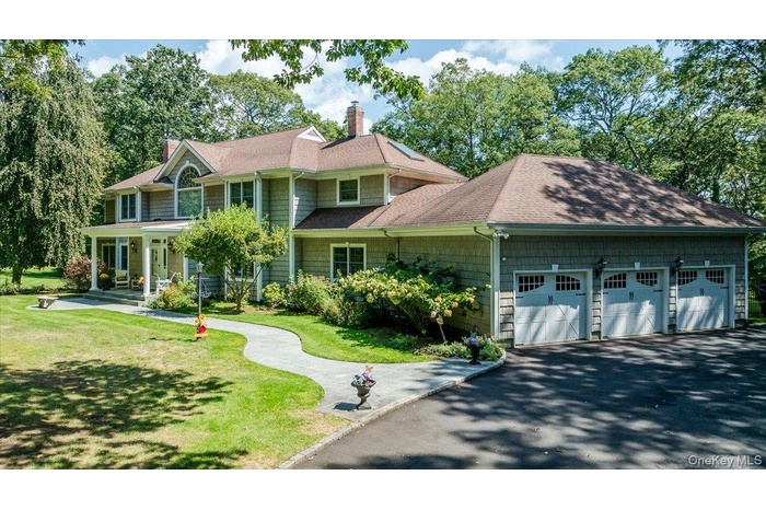 View of front of house with a front lawn, roof with shingles, a chimney, covered porch, and driveway