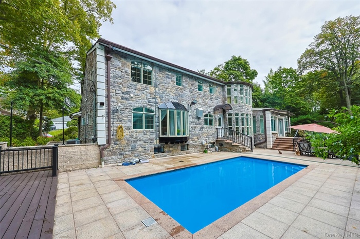Rear view of property featuring a patio area, stone siding, and an outdoor pool