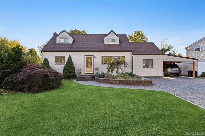 Cape cod home with an attached carport, a front yard, decorative driveway, roof with shingles, and a chimney