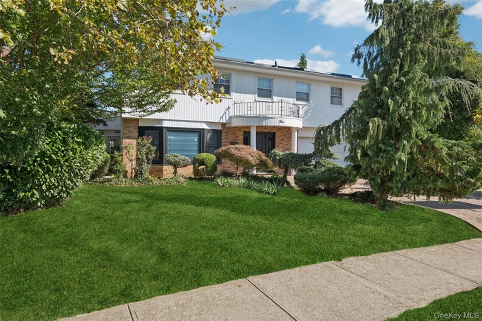 View of front of home with brick siding, a front yard, and a balcony