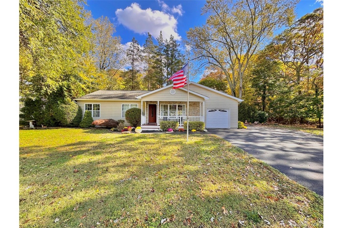 View of front of house with driveway, covered porch, a front yard, and an attached garage