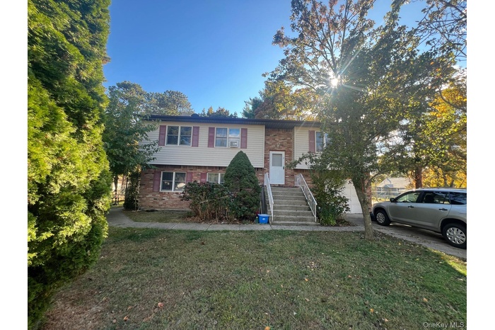 Raised ranch with brick siding, a front yard, an attached garage, and driveway