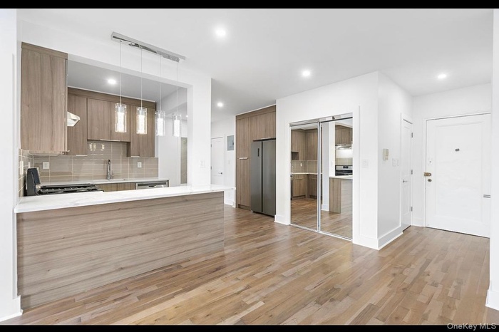 Kitchen featuring modern cabinets, tasteful backsplash, a peninsula, light wood-style flooring, and decorative light fixtures