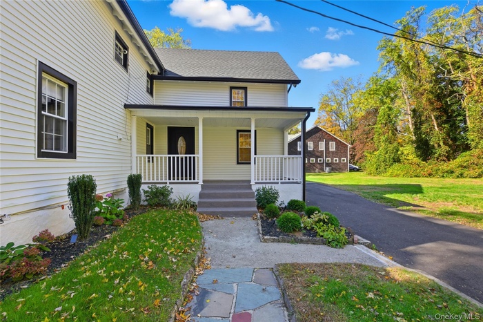 Entrance to property featuring covered porch, roof with shingles, and a yard