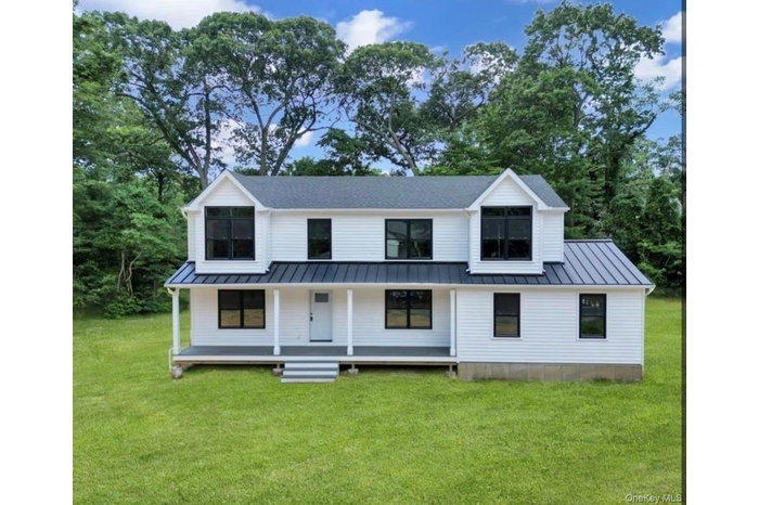 Modern farmhouse with covered porch, a standing seam roof, a metal roof, and a front lawn
