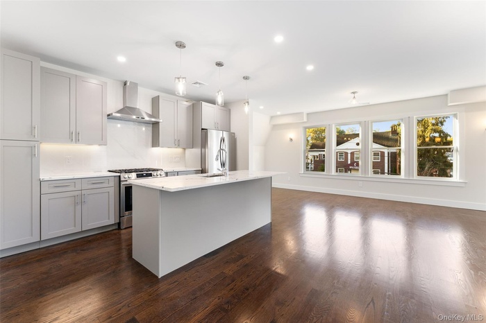 Kitchen with appliances with stainless steel finishes, wall chimney range hood, recessed lighting, dark wood-style floors, and a center island with si