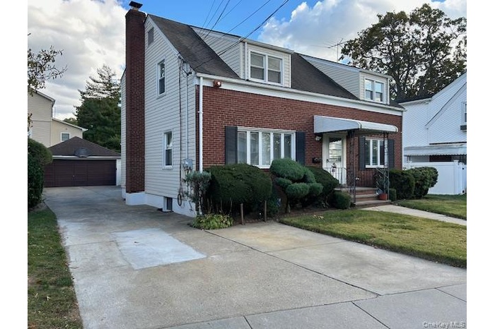 View of front of property featuring an outbuilding, brick siding, a front lawn, a garage, and a chimney