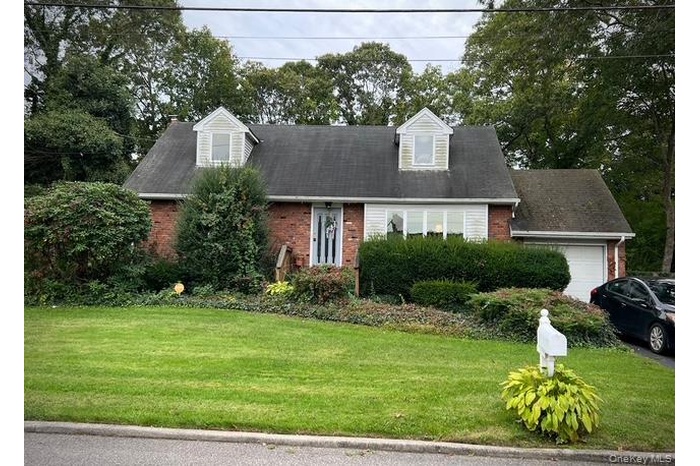 Cape cod house featuring brick siding, a front lawn, and an attached garage