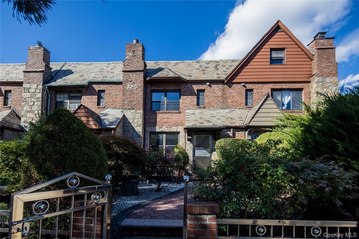 English style home with a high end roof, a chimney, brick siding, a gate, and stone siding