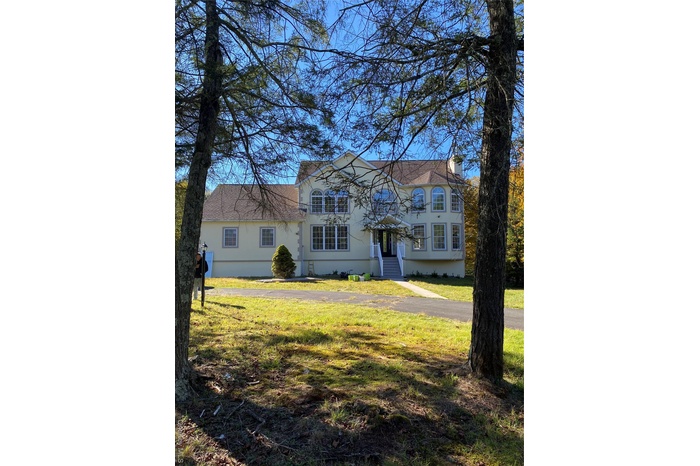 View of front facade with a front lawn, roof with shingles, stucco siding, and a chimney
